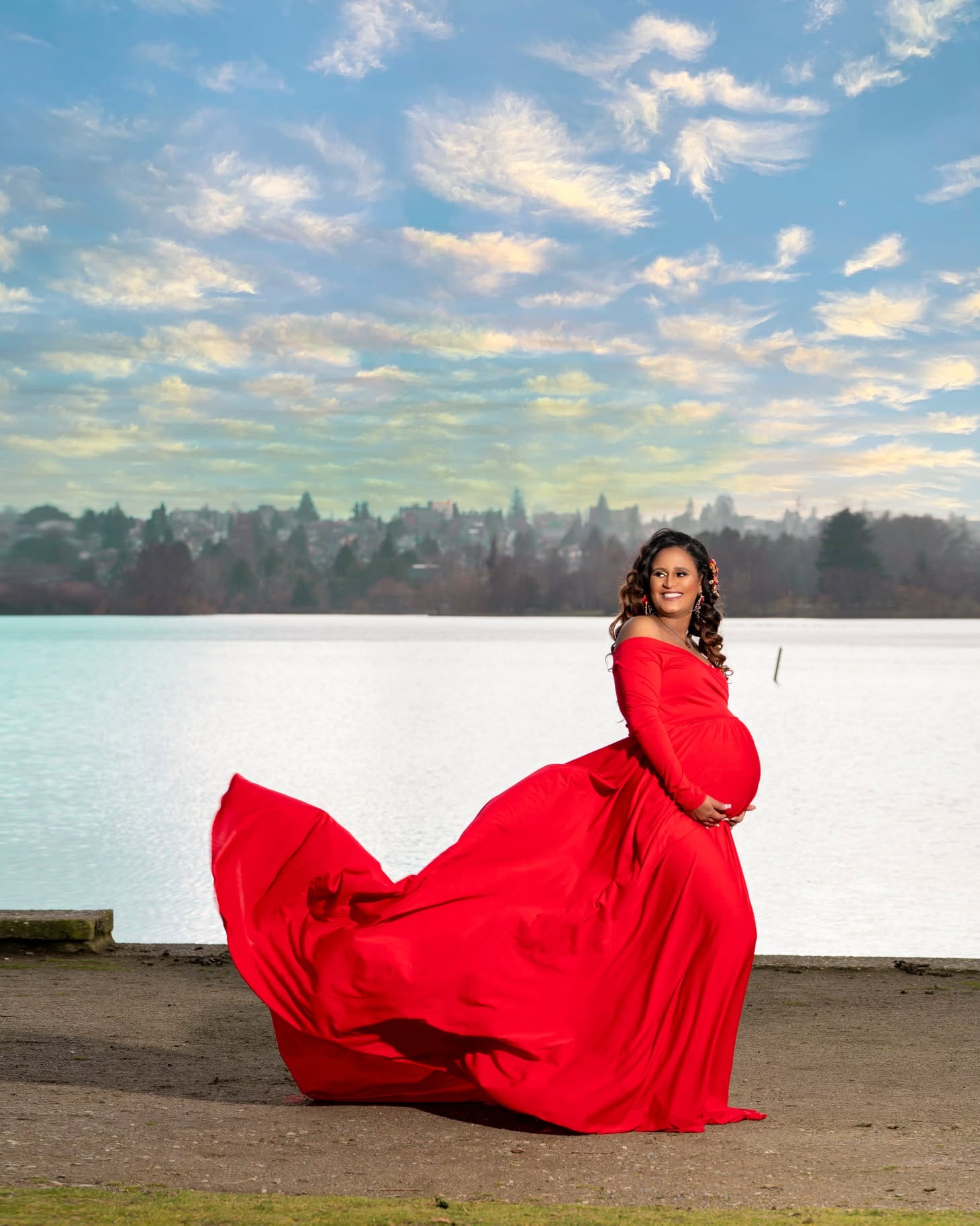 Maternity portrait in a flowing red dress by the lake